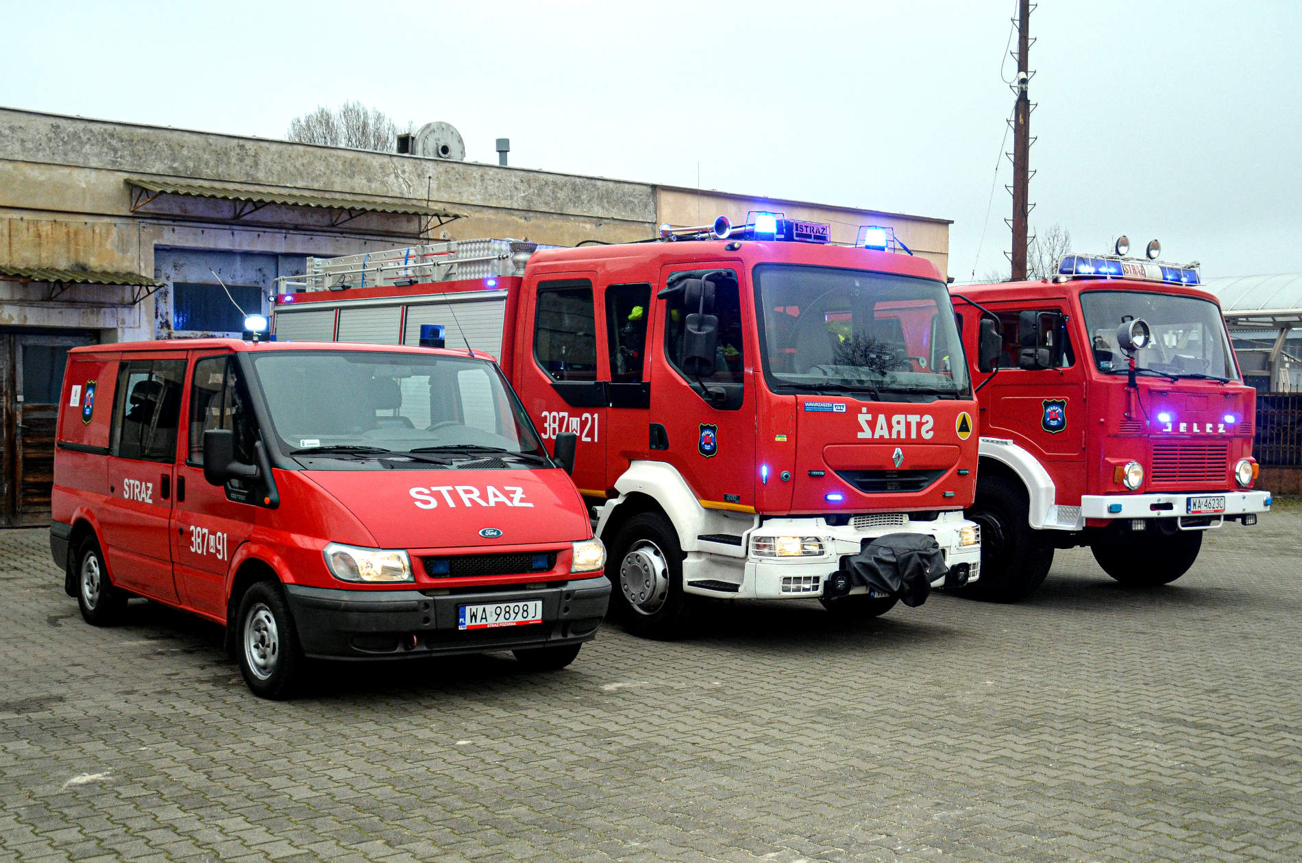 Trzy czerwone pojazdy strażackie z OSP Warszawa Białołęka z napisem „STRAŻ” stoją przed budynkiem przy ul. Dorodnej 16 w Warszawie Białołęce.